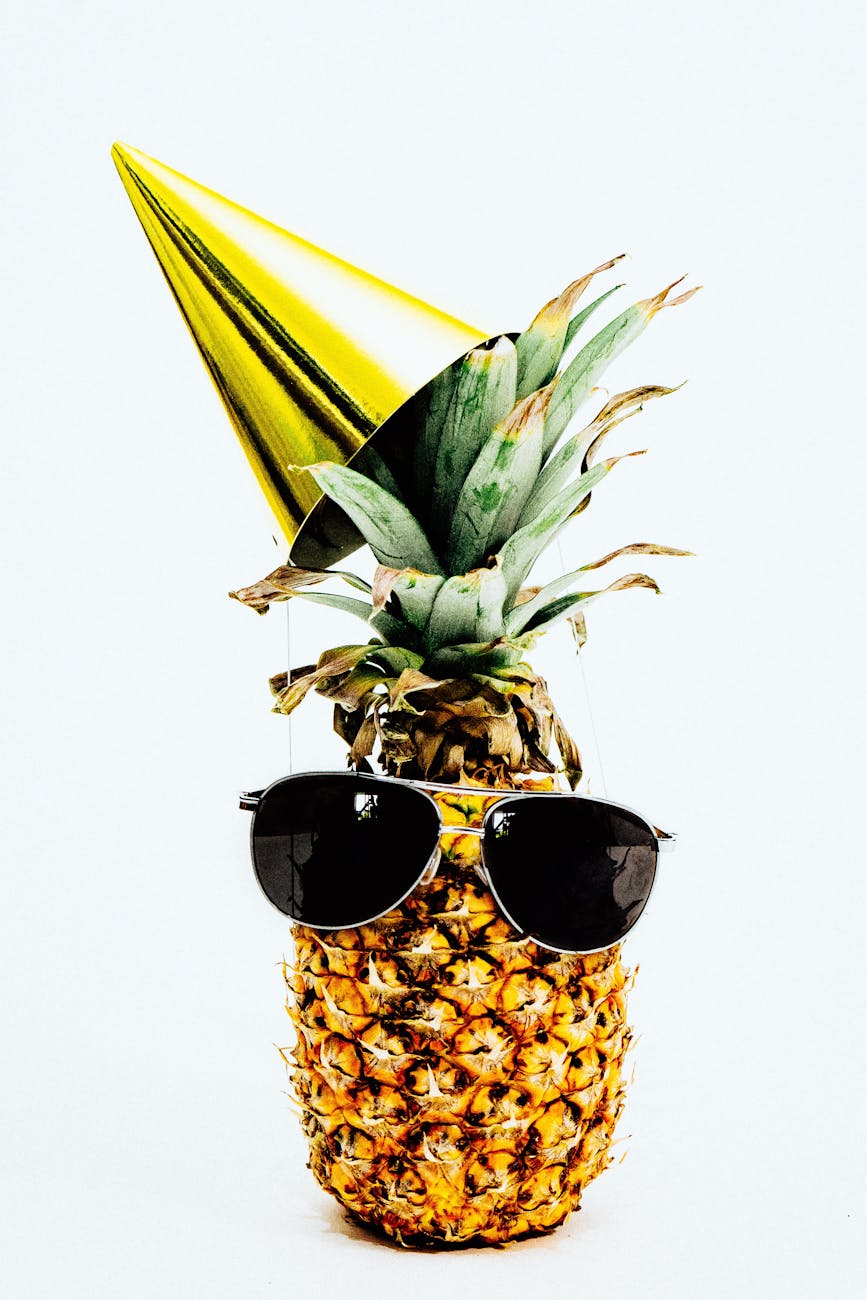 close up photo of pineapple with party hat and a black sunglasses